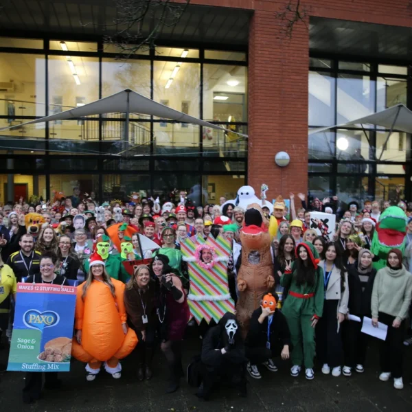 A large group of people gathered outside a building for a fun event, some wearing costumes and holding signs.