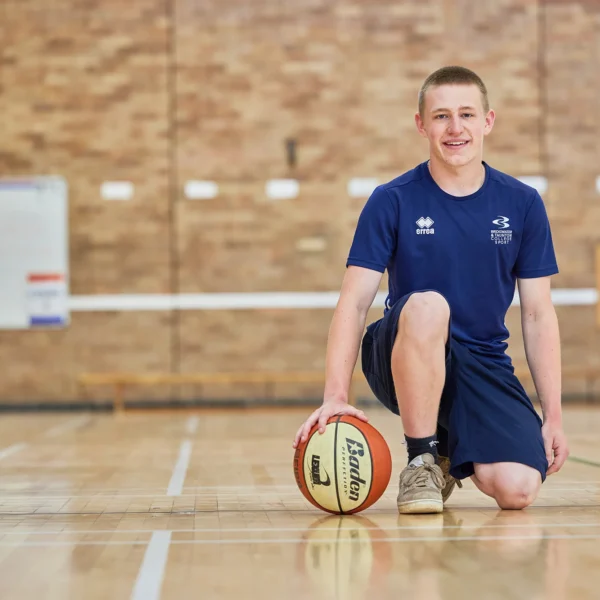 A man kneeling on a basketball court with a ball.