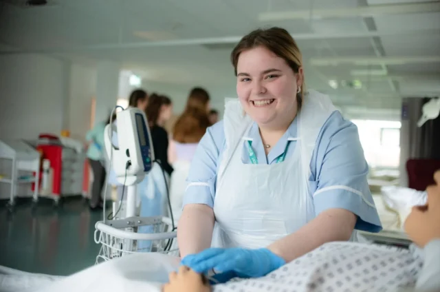 Nurse trainee practicing on a mannequin patient in a simulated hospital environment