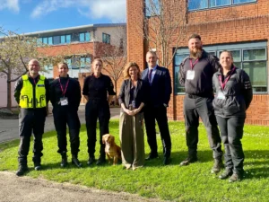 A group of people standing on grass in front of a building with a dog, likely a police or security team.