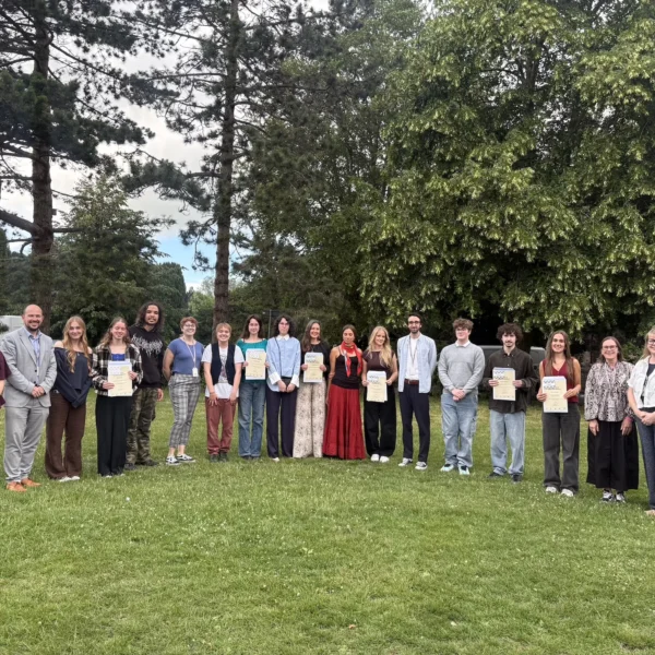 Group of people standing in a line on grass holding certificates, smiling and looking at the camera.