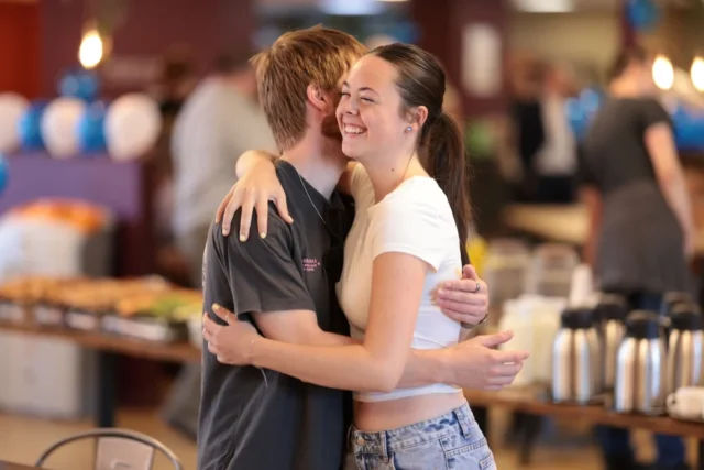 A group of young adults hugging and smiling at a school or community event.
