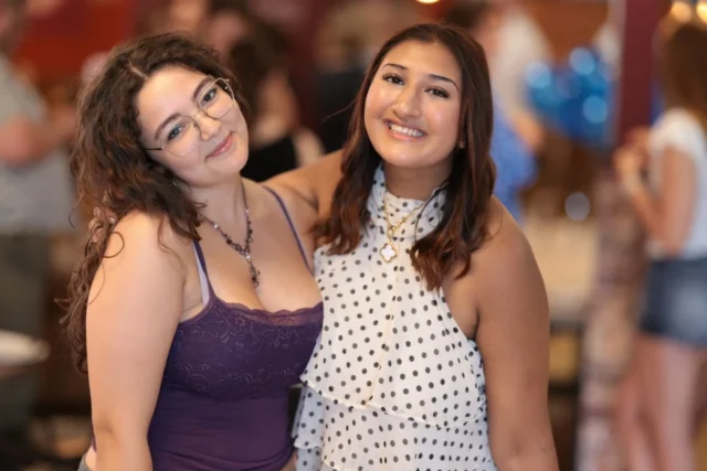 Two smiling women standing close together at a social event.
