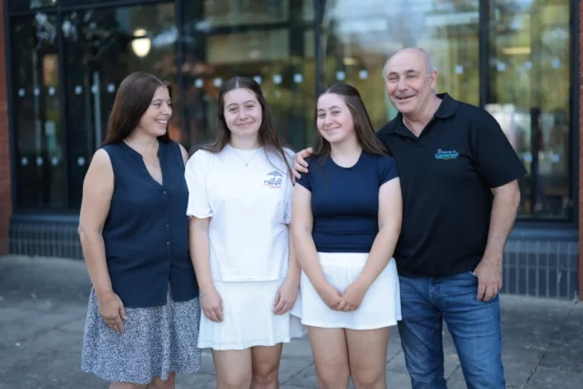A smiling family stands together outside a storefront, showcasing a friendly and welcoming atmosphere.