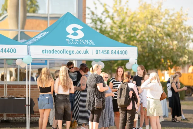 Stroud College students gather under a promotional tent at an outdoor event, engaging in conversations and networking.