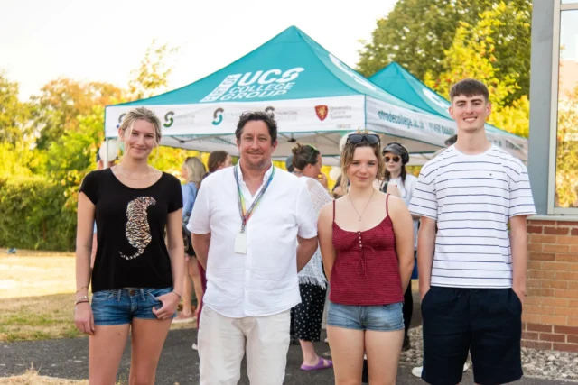 A group of smiling individuals stands in front of a UCG-branded tent at an outdoor event.