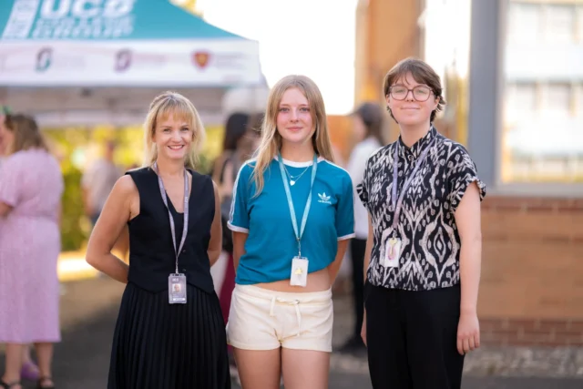 Three smiling individuals standing together outdoors, likely at a community event or educational setting.