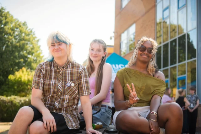Three friends sitting together outside a modern building, enjoying a sunny day.