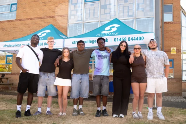 A group of students standing together outside Stride College during an event under a branded tent.
