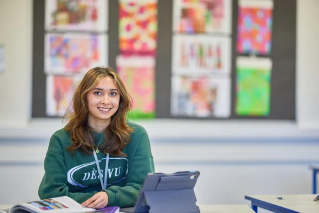 A young girl sitting at a desk with an iPad.