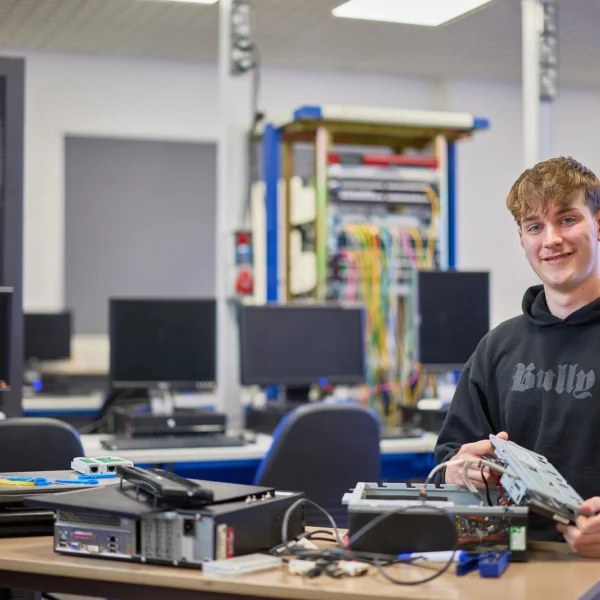 A young man in a black hoodie working on computer hardware in a classroom setting.