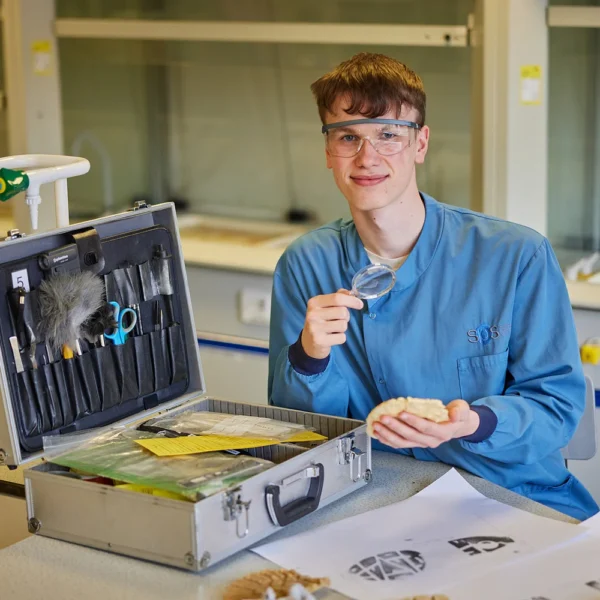Young man in a lab holding a tool and smiling.
