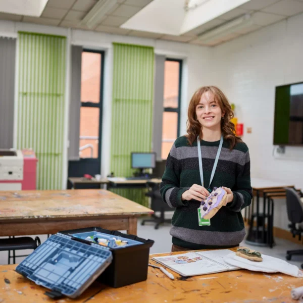 A smiling woman standing in a classroom with a lanyard around her neck.