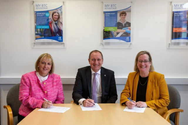 Three people sitting at a table signing documents