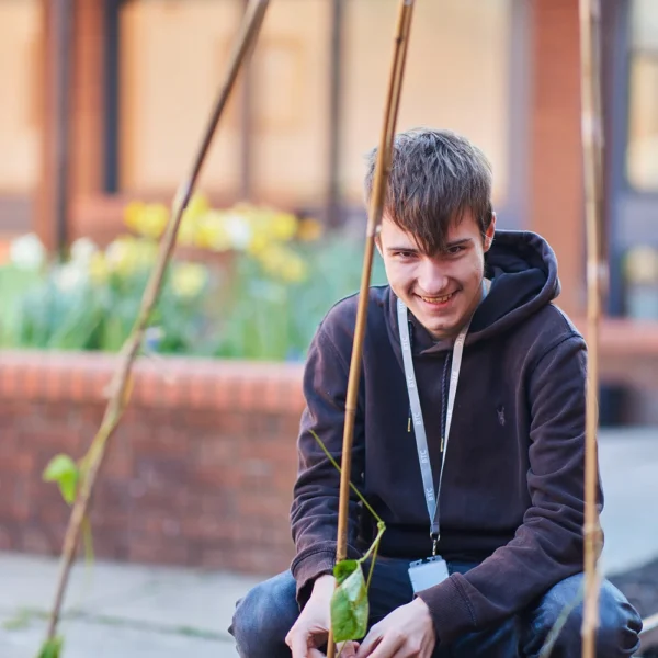Young man kneeling in garden with plant.