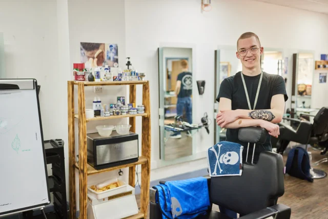 Man standing in a barber shop with his arms crossed.
