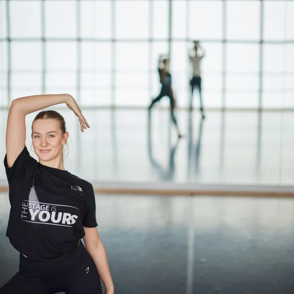A young dancer in a black shirt poses in a studio.