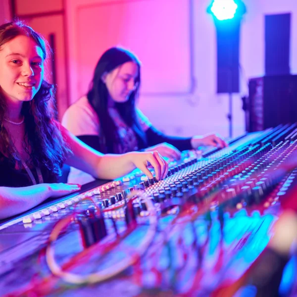 Two women working at a soundboard with blue and red lighting.