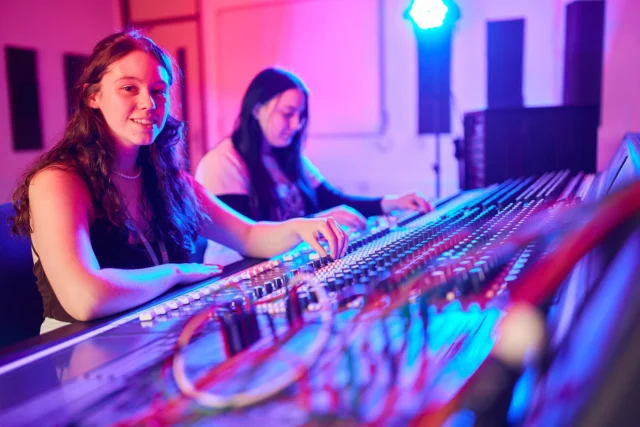 Two women working at a soundboard with blue and red lighting.