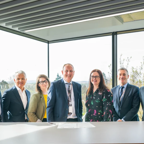 A group of seven business professionals standing around a table in a modern office with large windows.
