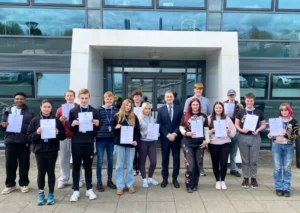 A group of young people holding certificates standing outside a modern building.