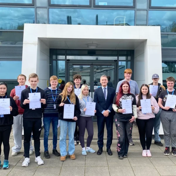 A group of young people holding certificates standing outside a modern building.