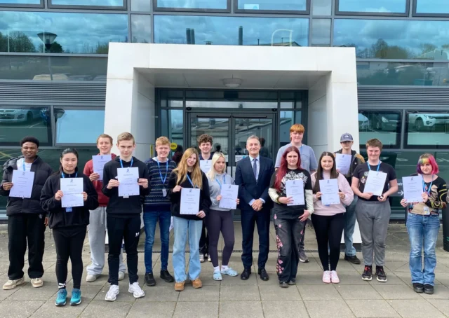 A group of young people holding certificates standing outside a modern building.