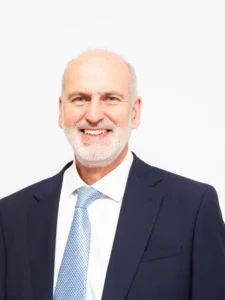 A smiling middle-aged man in a navy suit and light blue tie.