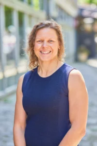 A middle-aged woman with shoulder-length brown hair smiles warmly while wearing a navy blue sleeveless top.
