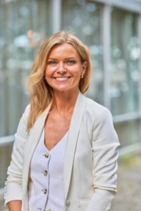 Blonde woman in a white blazer smiling at the camera.