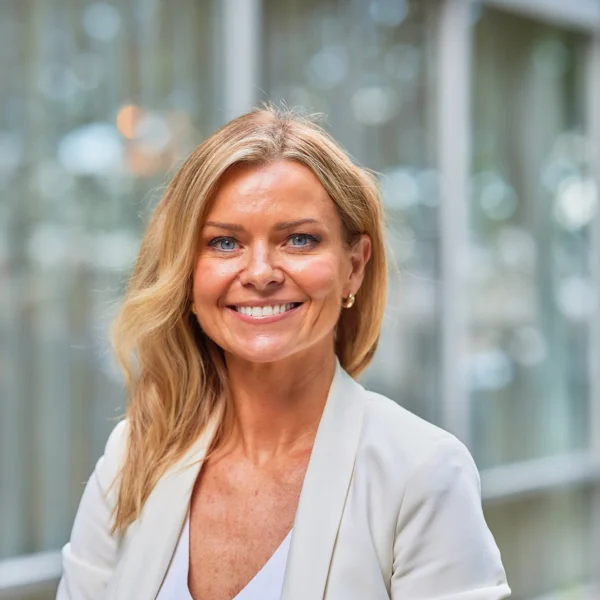 Blonde woman in a white blazer smiling at the camera.