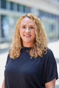 Portrait of a smiling woman with curly blonde hair wearing a black shirt.