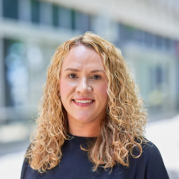 Portrait of a smiling woman with curly blonde hair wearing a black shirt.