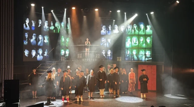 group of people performing on a stage with a large screen behind them