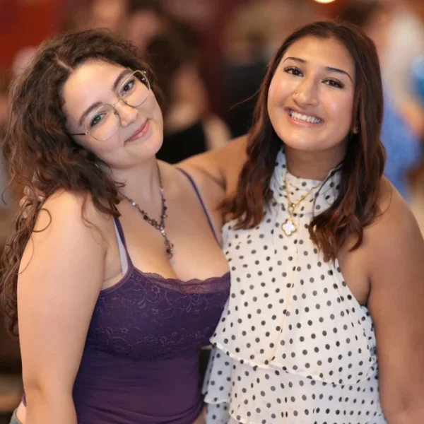 Two smiling women standing close together at a social event.