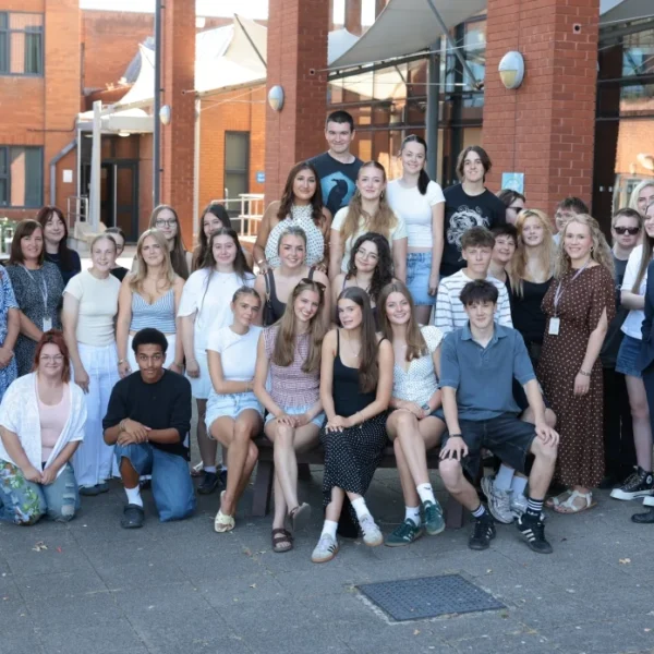 A large group of young people and adults posing together outside a red brick building, with a man in a suit standing on the right.