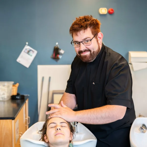 A professional hairdresser with a beard and glasses is washing a client's hair in a salon setting, while another image shows the same hairdresser smiling.