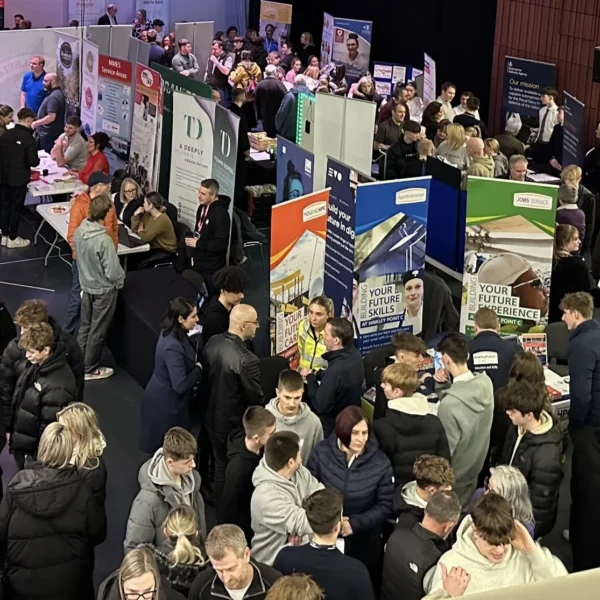 A large crowd of people at an indoor event or exhibition, with various booths and displays.