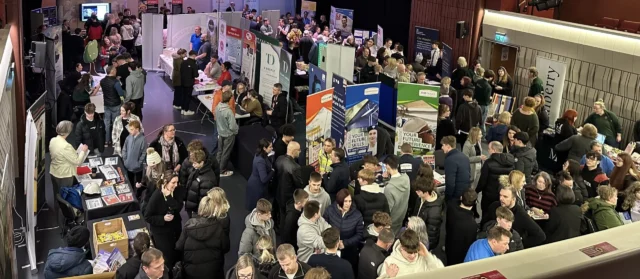 A large crowd of people at an indoor event or exhibition, with various booths and displays.