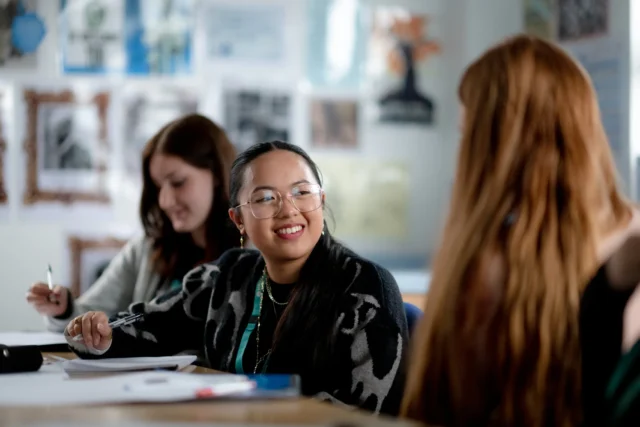 Two young women and a girl sitting at a table in a classroom setting.