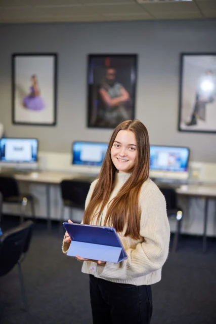 A young woman with long brown hair holding a folder in a computer lab.