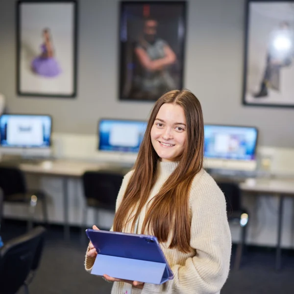 A young woman with long brown hair holding a folder in a computer lab.