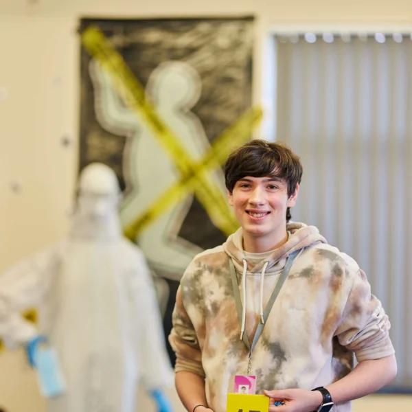 A young man wearing a tie-dye hoodie holds a yellow sign with the number 15.
