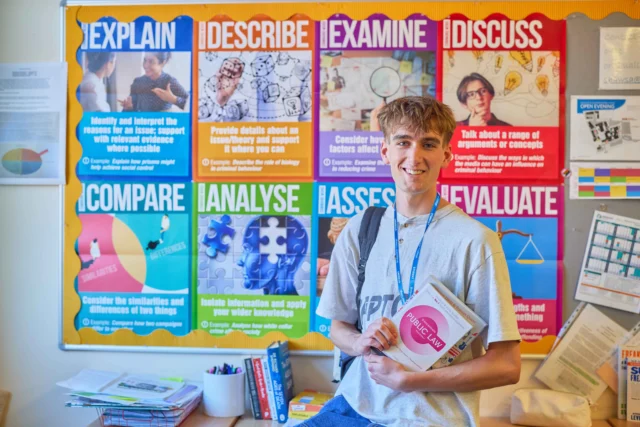 Young boy holding books standing in front of educational wall posters