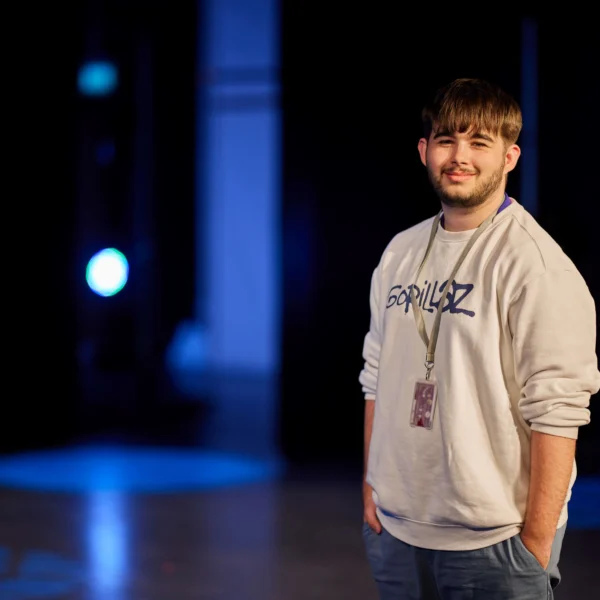 Young man wearing a grey sweatshirt and lanyard standing on a stage.