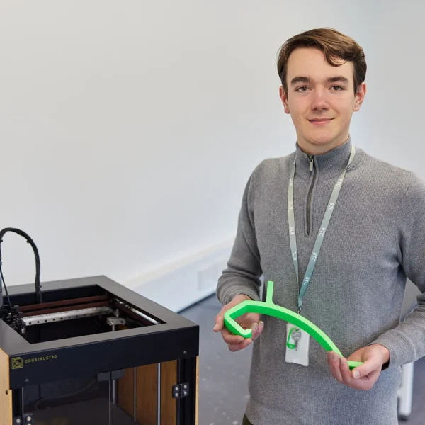 Young man holding a green 3D printed object next to a 3D printer