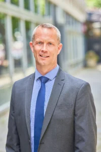 A professional man in a grey suit standing outside a modern building.