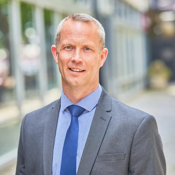 A professional man in a grey suit standing outside a modern building.