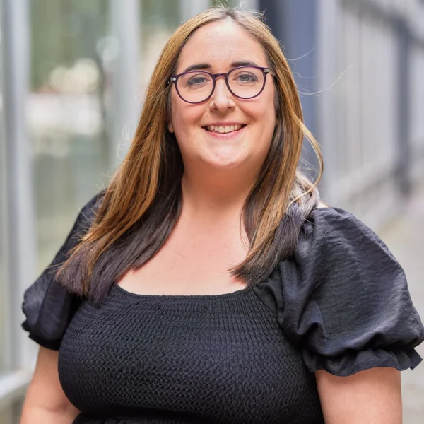 A smiling woman with long brown hair and black glasses wearing a black dress