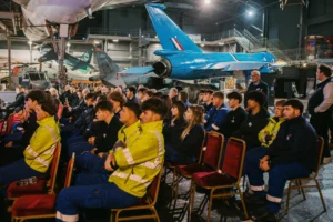 A group of people sitting in chairs in front of an airplane.